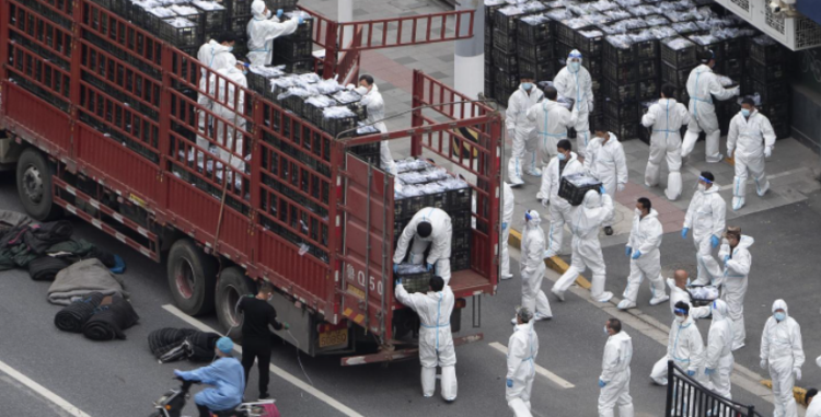 Workers in PPE unload groceries from a truck before distributing them to local residents under the COVID-19 lockdown in Shanghai, China, on April 5, 2022.