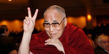 FILE - The Dalai Lama directs a peace sign toward the head table, where U.S. President Barack Obama was seated, during the National Prayer Breakfast in Washington, Feb. 5, 2015.