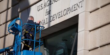 A worker removes the U.S. Agency for International Development sign on their headquarters on Feb. 07, 2025 in Washington, D.C.