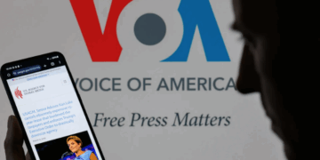 The U.S. Agency for Global Media website is displayed on a phone with Voice of America branding in the background. Photo: Jonathan Raa/NurPhoto via Getty Images