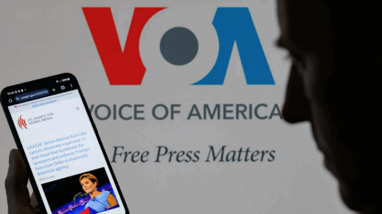 The U.S. Agency for Global Media website is displayed on a phone with Voice of America branding in the background. Photo: Jonathan Raa/NurPhoto via Getty Images